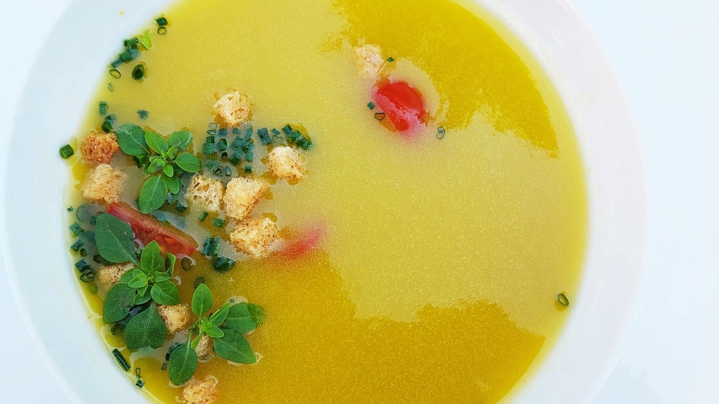 Kalte spanische Suppe: gelbe Gazpacho in einem weißen Teller mit Kräutern und Croutons als Einlage