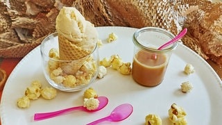 Eis mit Popcorn in einem Hörnchen und Karamellsauce im Glas daneben. Drumherum Popcorn