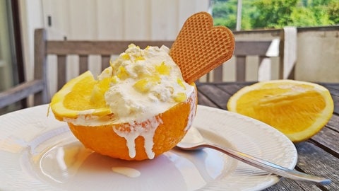 halbe Orange mit Eiscreme darin mit einer Waffel auf einem weißen Teller