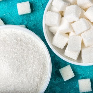 Zucker ist ungesund: Loser Zucker und Zuckerstückchen in Schüsseln aufgehäuft. 