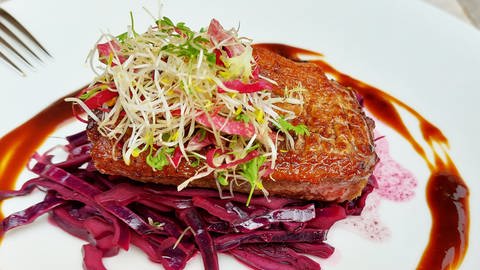 Rezept Entenbrust auf Rotkohl: ein Stück Entenbrust mit Salatbouquet auf Rotkohl auf einem weißen Teller mit Sauce drumherum