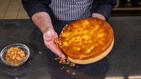 Der gebackene Apfel-Quitten-Kuchen wird mit der Hand am Rand mit gerösteten Mandeln dekoriert