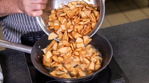 Die geschälten und geschnittenen Quitten werden aus einer Schüssel zum Dünsten in eine Pfanne mit Butter geschüttet.