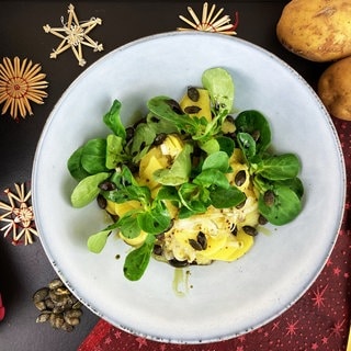 Rezept für Weihnachtsessen vegetarisch: Steirischer Kartoffelsalat mit Feldsalat und Kürbiskernen auf einem weißen Teller, daneben Weihnachtssterne und Kartoffeln