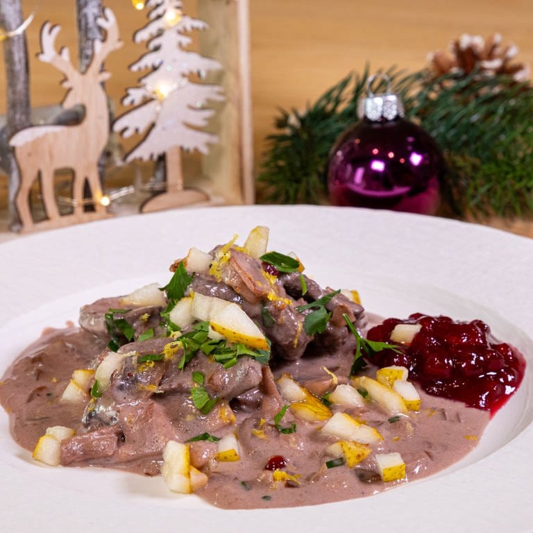 Festliches Hirschragout zu Weihnachten mit Preiselbeeren und Birne schön angerichtet auf einem Teller.