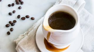 Rezept für Süße Sauce aus Kaffee mit Rum. In einer weißen Karaffe ist dunkle Sauce, daneben liegen Kaffeebohnen.
