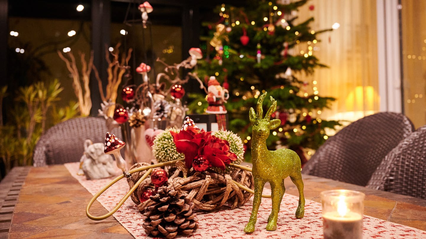 Weihnachtsdeko auf Tisch mit Weihnachtsbaum im Hintergrund.