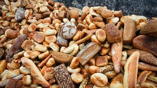 Viele alte Brötchen und Brotlaibe liegen auf einem großen Haufen vor einer Mauer. 