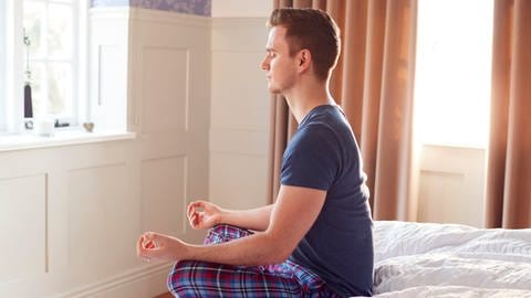 Mann macht Meditation im Bett. Tipps, um besser aus dem Bett zu kommen.