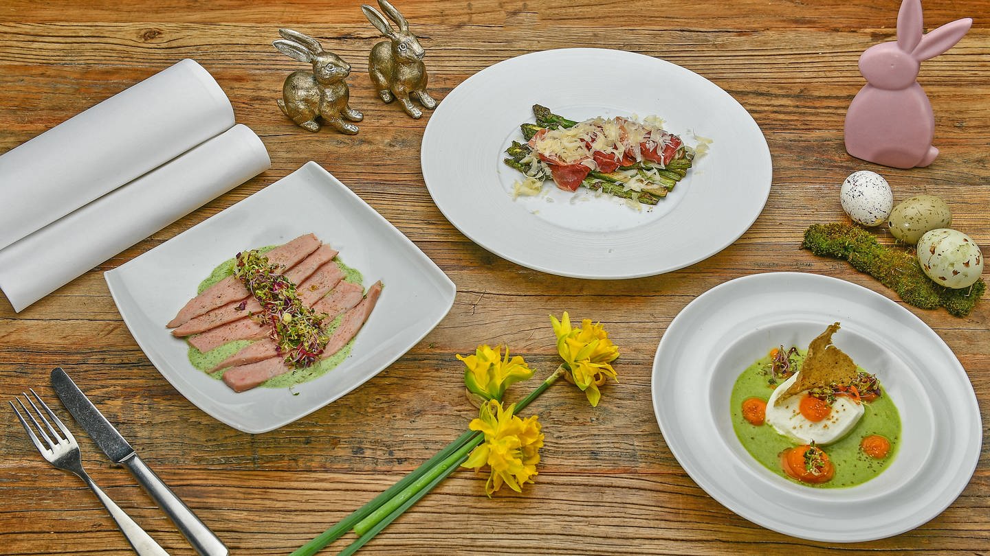 Holztisch mit 3 Gerichten darauf: kalbsfleisch mit grüner Sauce, Mozzarella mit grünem Sud und Süßkartoffelpüree, grüner Spargel mit Schinken und Parmesan, daneben Osterdeko