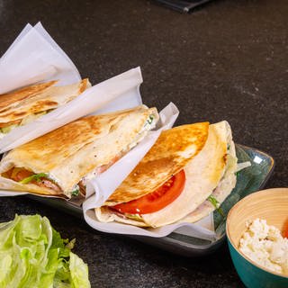 Rezept für Tortilla-Sandwich: Die frisch angerichteten Tortilla-Sandwiches, eingepackt in Brotpapier und verzehrfertig als Fingerfood.