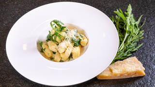 Leckeres und vegetarisches Rezept für italienische Gnocchis mit Parmesan und Rucola: Das Gericht ist auf einem weißen Teller angerichtet.