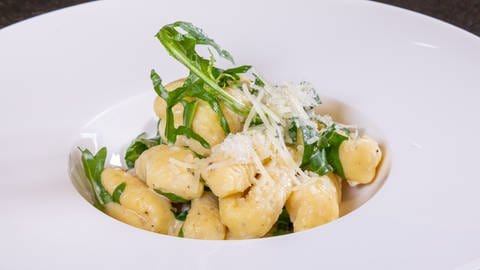 Selbstgemachte Gnocchi mit einer leckeren Soße aus cremigem Parmesan und Ruccola – angerichtet auf einem weißen Teller.