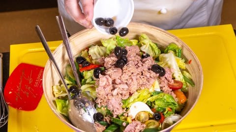 Dem Nizzasalat werden, wie im Rezept beschrieben, neben Ei und Thunfisch auch schwarze Oliven zugegeben. 