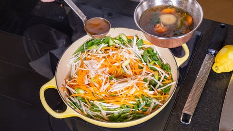 Das Gemüse für den Lachs wird in einer Pfanne mit Brühe abgelöscht.