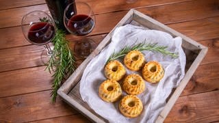 Gugelhupf herzhaft mit Gemüse als kleine Kuchen arrangiert neben einer Flasche und zwei Gläsern Rotwein und Rosmarin-Stängeln.