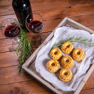 Gugelhupf herzhaft mit Gemüse als kleine Kuchen arrangiert neben einer Flasche und zwei Gläsern Rotwein und Rosmarin-Stängeln.