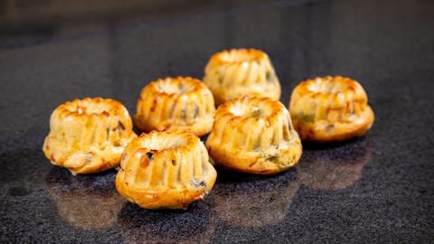 Die goldgelb bebackenen kleinen Kuchen liegen zum Abkühlen auf der Arbeitsplatte – fertig ist der Gugelhupf in herzhaft mit Gemüse.