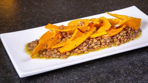 Karamellisierter Butternut-Kürbis ist auf einem Salat aus Alblinsen in einer weißen Schale angerichtet.