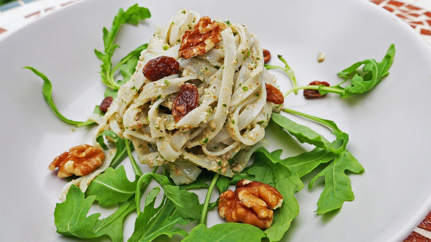 Helle Bandnudeln mit Walnuss-Pesto, Walnüssen und getrockneten Beeren auf Rucola-Blättern