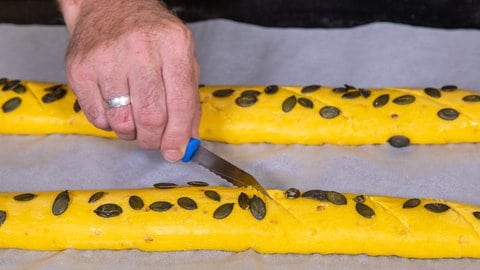 Wie im Rezept beschrieben, werden mit einem Messer die Baguette eingeschnitten. Dann mit Wasser bestreichen und mit Kürbnis-Kernen bestreuen. Die tolle Farbe hat da Baguette durch den Hokkaido.