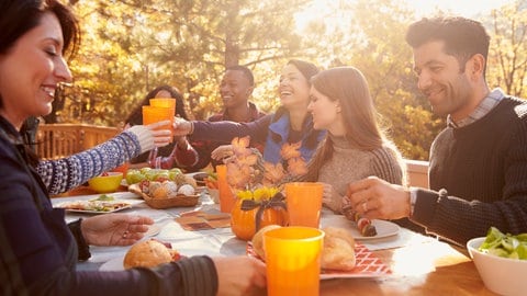 Tipps gegen Herbstblues: Mehrere Freunde sitzen an einem herbstlich gedeckten Tisch und essen zusammen.