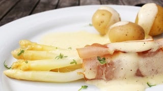 Rezept für Spargel mit Schinken und Sauce Hollandaise: Schön angerichteter Spargel mit den Beilagen und der Soße auf einem Teller