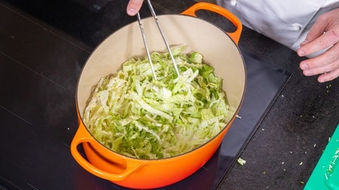 Geschnittener Wirsing im Topf mit Brühe, Sahne und Zwiebeln: Das Gemüse sollte zugedeckt fünf bis sieben Minuten garen. Dafür einfach den Deckel auf den Topf setzen!