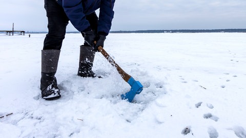 Ein Mann schlägt mit einer Axt ein Loch in eine Eisdecke: Was für das Eisfischen sinnvoll ist, ist nicht ratsam bei einem Teich, in dem Fische und andere Tiere leben. Sie können durch die Druckwellen Schaden nehmen.