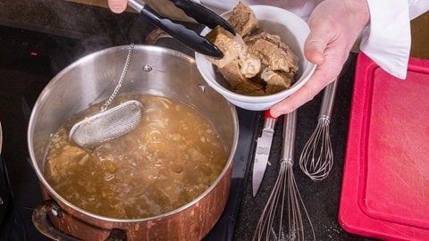 Die Kalbfleisch-Stücke werden mit einer Zange aus dem Sud geholt.