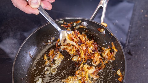 Zwiebeln werden in einer Pfanne angebraten. Sie geben dem Eintopf den Kick und werden am Ende als Topping dem Gaisburger Marsch zugegeben.