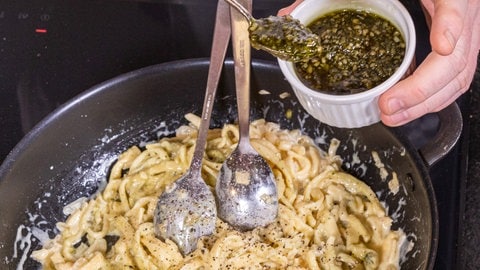 Pesto wird Spätzle hinzugefügt, die sich in einer Pfanne befinden. 