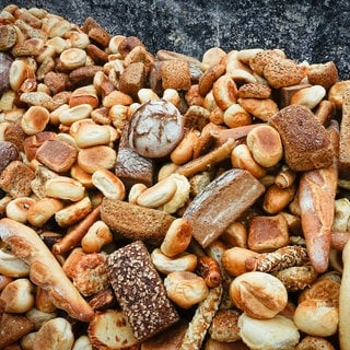 Viele alte Brötchen und Brotlaibe liegen auf einem großen Haufen vor einer Mauer. 