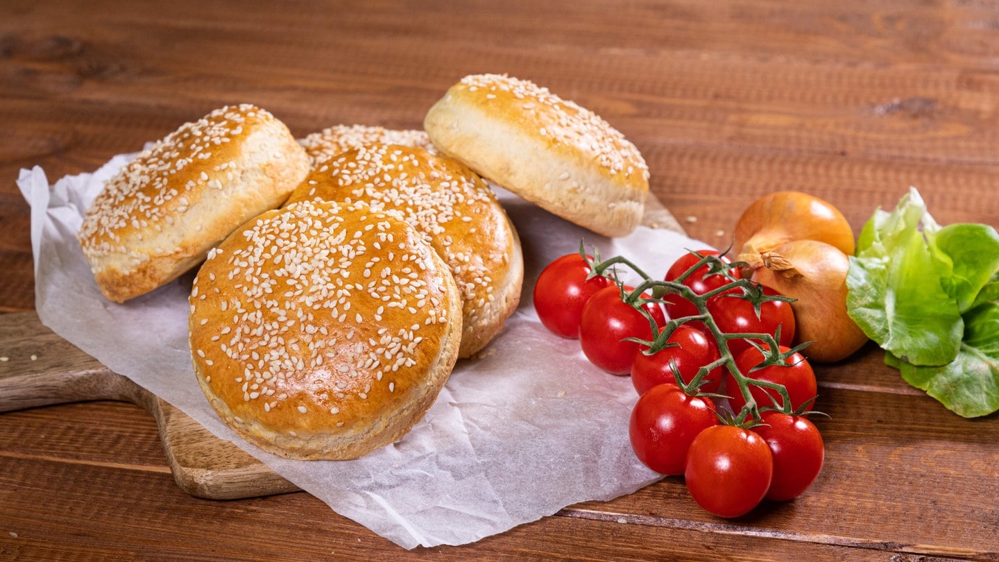 Rezept Burgerbrötchen selber machen: Die fertig gebackenen Burgerbrötchen auf einem Holzbrett.