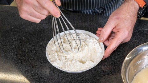 Leckeres Rezept für Ananas-Kokos-Kuchen: Mehl, Backpulver und Natron werden in einer kleinen, weißen Schüssel miteinander vermischt