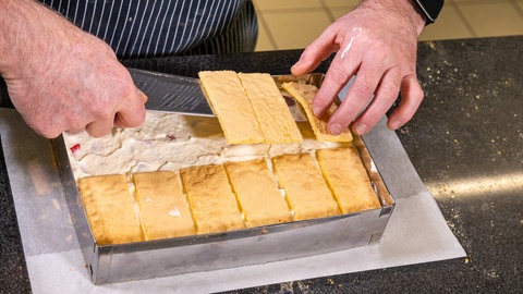 Erdbeer-Sahne-Schnitten backen: Der Biskuitteig wird in zugeschnittenen Portionen auf die Sahne-Creme gelegt. 