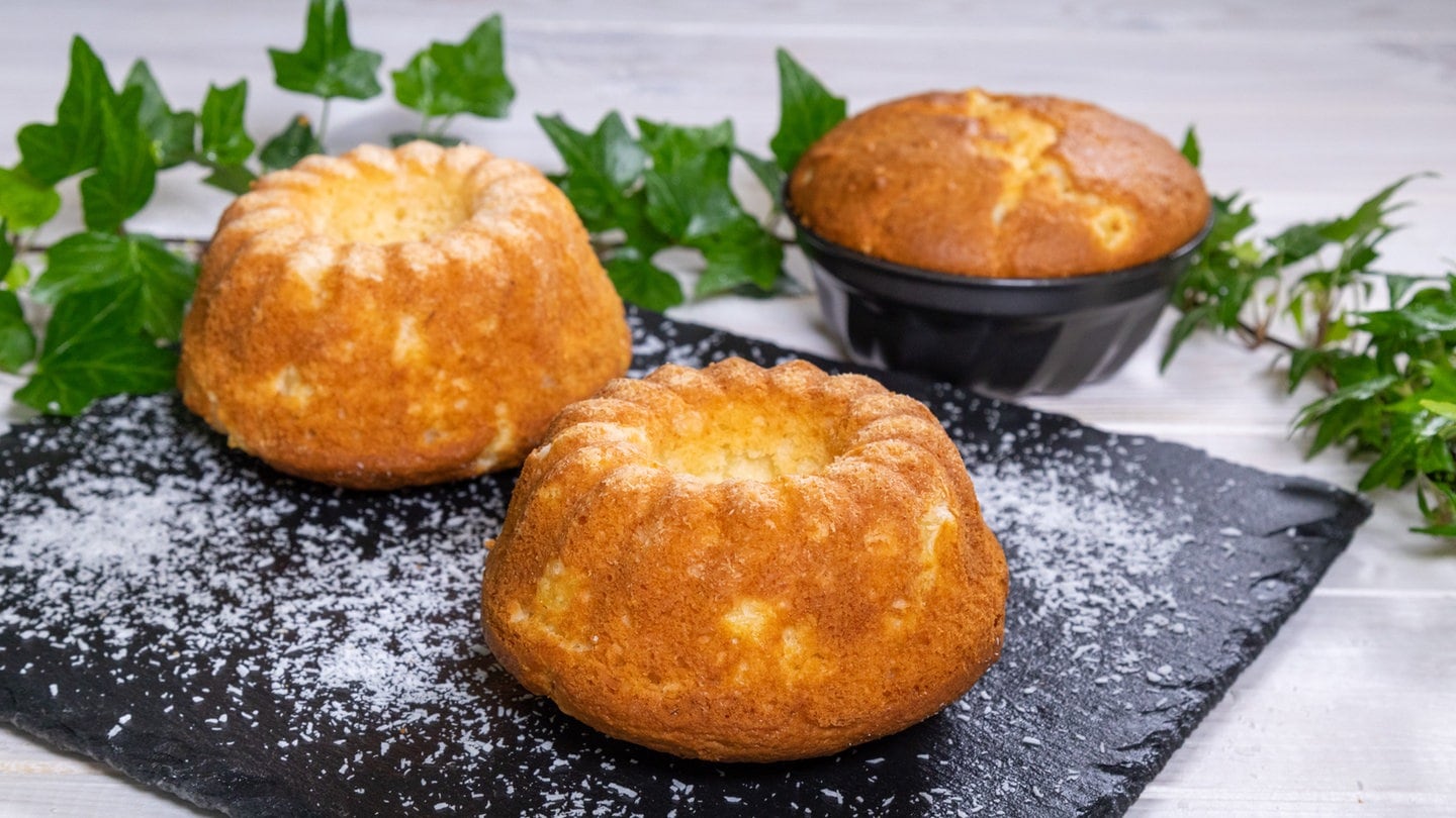 Leckeres Rezept für Ananas-Kokos-Cake: drei kleine Kuchen serviert auf einer dunklen Steinplatte. Ein Küchlein ist noch in einer schwarzen Form.