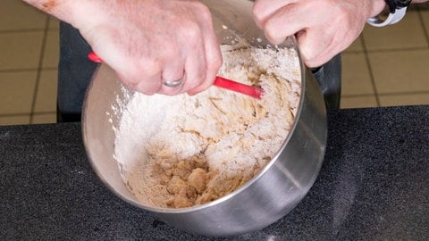 Mit einem Löffel wird ganz schnell und einfach die Trockenmischung in den Teig für die Rhabarberschnitte gerührt.