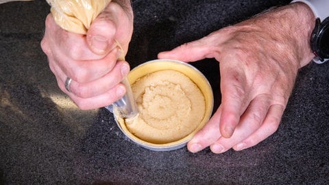 Pfirsichtartelettes backen: Die Marzipanfüllung auf dem Mürbeteig platzieren.