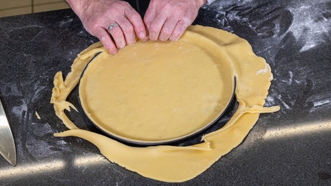 Der Mürbeteigboden für die erfrischende Zitronentarte wird erst ausgerollt und dann ganz einfach auf dem Backblech gelegt.