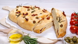 Perfekt als Beilage zum Grillen: Focaccia aus fluffigem Teig, Oliven, getrockneten Tomaten und italienischen Kräutern