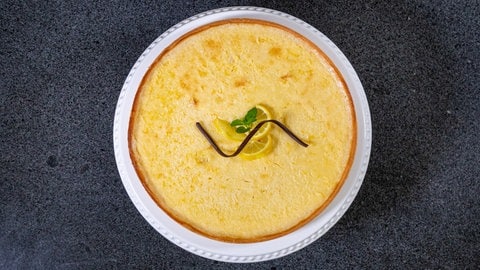 Die Zitronentarte ist frisch gebacken und liegt auf einer Tortenplatte. Die Tarte ist erfrischend und mit Zitronenscheiben lecker dekoriert.