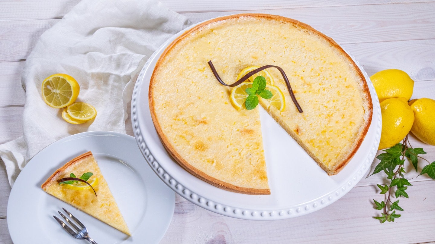 Die fertige Zitronentarte ist angeschnitten und ein Stück von dem Kuchen ist neben der erfrischend und leckeren Tarte auf einem Teller angerichtet.