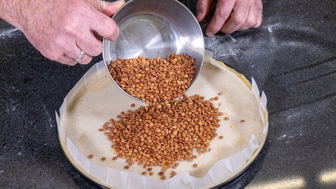 Der Mürbeteigboden der Zitronentarte wird vor dem Backen ganz einfach mit Backpapier belegt und mit Hülsenfrüchten aufgefüllt.