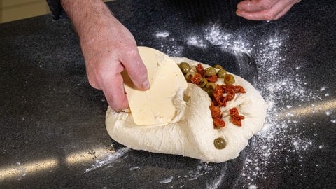 Italienisches Focaccia Rezept: Die Oliven und getrockneten Tomaten in die Mitte des Teigs einarbeiten.