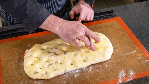 Italienisches Focaccia Rezept: Den Teig mit der Füllung langziehen und kleine Vertiefungen auf der Oberseite eindrücken.