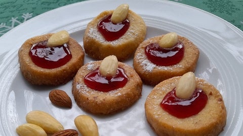 Rezept für Husarenkrapfen: Mehrere Plätzchen liegen zusammen mit ein paar Mandeln auf einem weißen Teller.