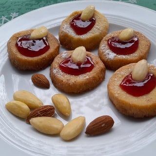 Rezept für Husarenkrapfen: Mehrere Plätzchen liegen zusammen mit ein paar Mandeln auf einem weißen Teller.