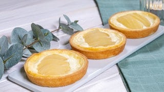 Rezept für Birnen-Tartelettes: Die kleinen Törtchen mit Birne und Quark auf einem Teller angerichtet.