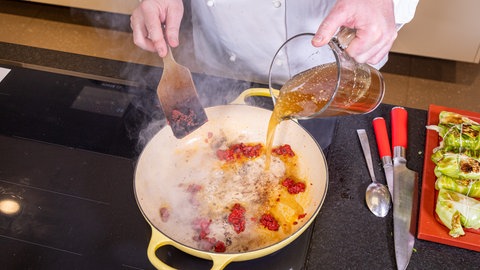 Rezept Kohlrouladen mit Hackfleisch: Der Koch macht mit dem Butterschmalz, Tomatenmark und einer Brühe die Soße in einer Pfanne.